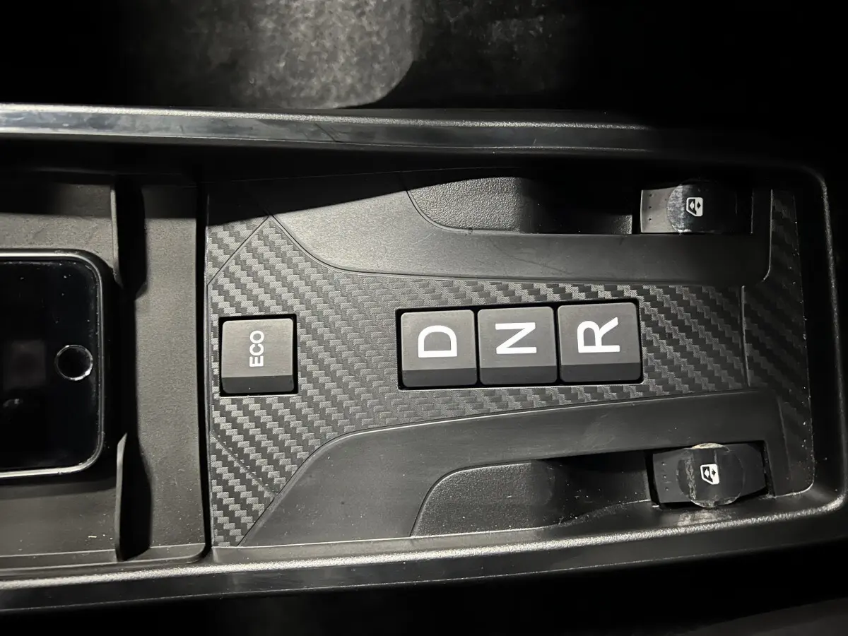 Gros plan sur la console centrale noire à effet carbone de la Ligier JS50 BEV 8KWH ELITE avec boutons de boîte auto et commandes vitres.