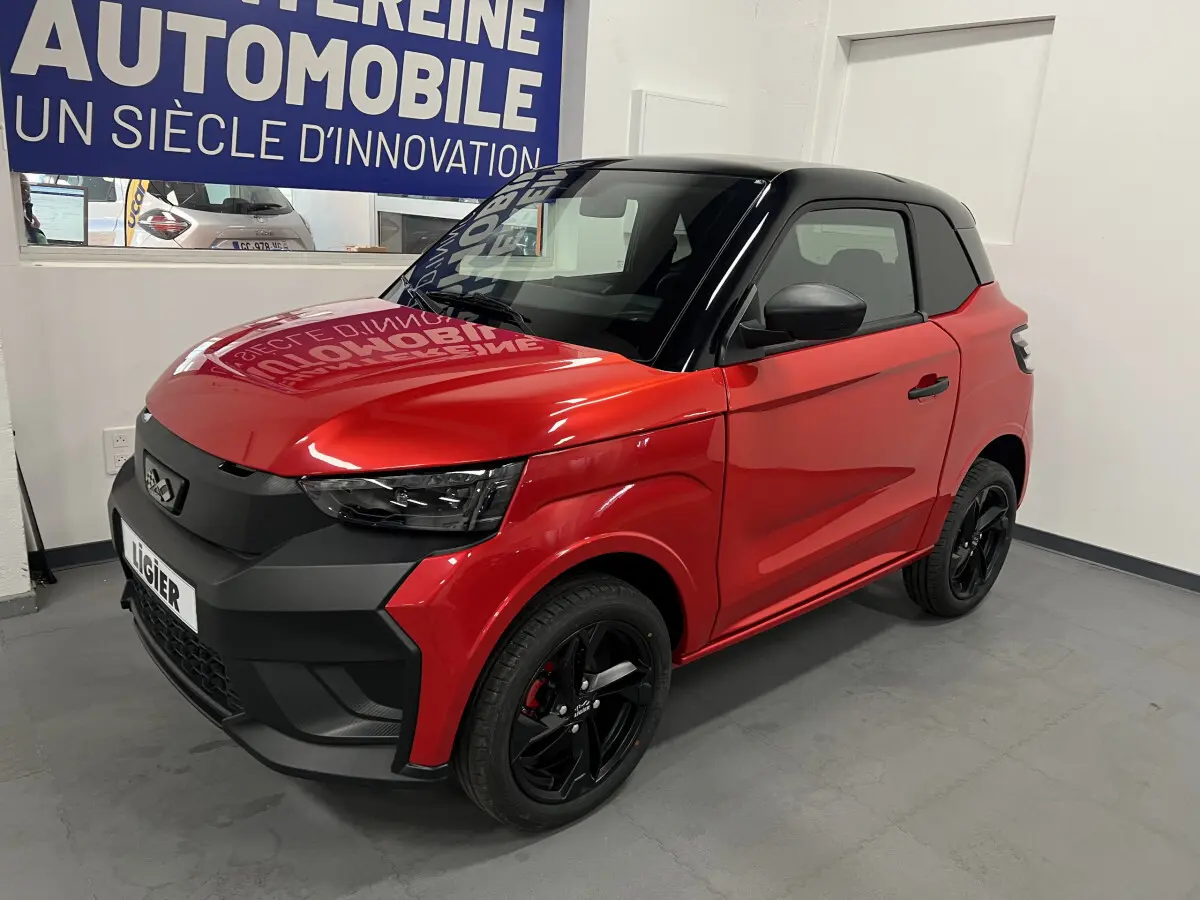 Vue 3/4 avant d'une LIGIER JS50 BEV 8KWH ELITE rouge avec toit noir et jantes alu noires en intérieur showroom.