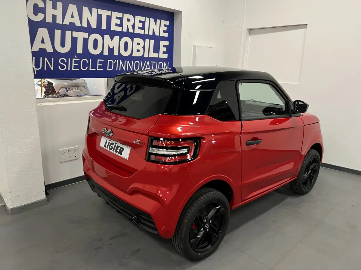 Vue 3/4 arrière droite de la LIGIER JS50 BEV 8KWH ELITE rouge avec toit noir et jantes alu noires en intérieur showroom.