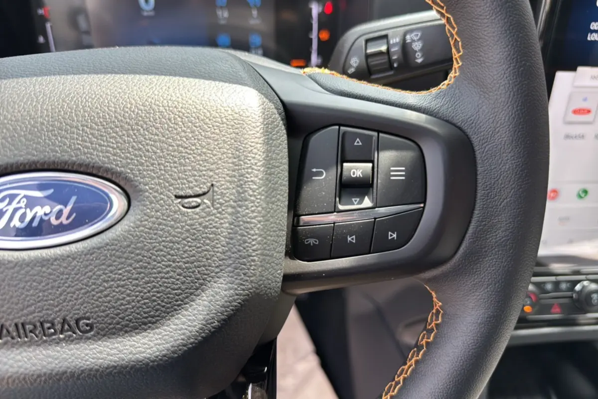 Gros plan sur le volant en cuir noir avec surpiqûres orange du Ford Ranger 2025, boutons multifonctions visibles.