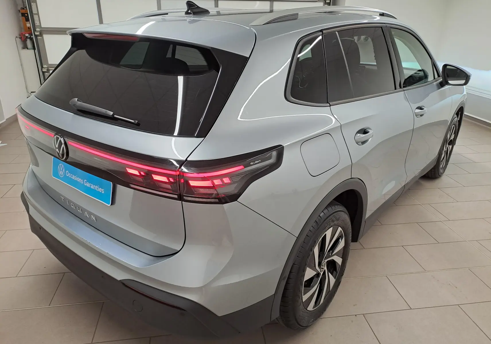 Vue 3/4 arrière droite du Volkswagen Tiguan 2025 en argent Dolomite avec feux arrière allumés dans un showroom.