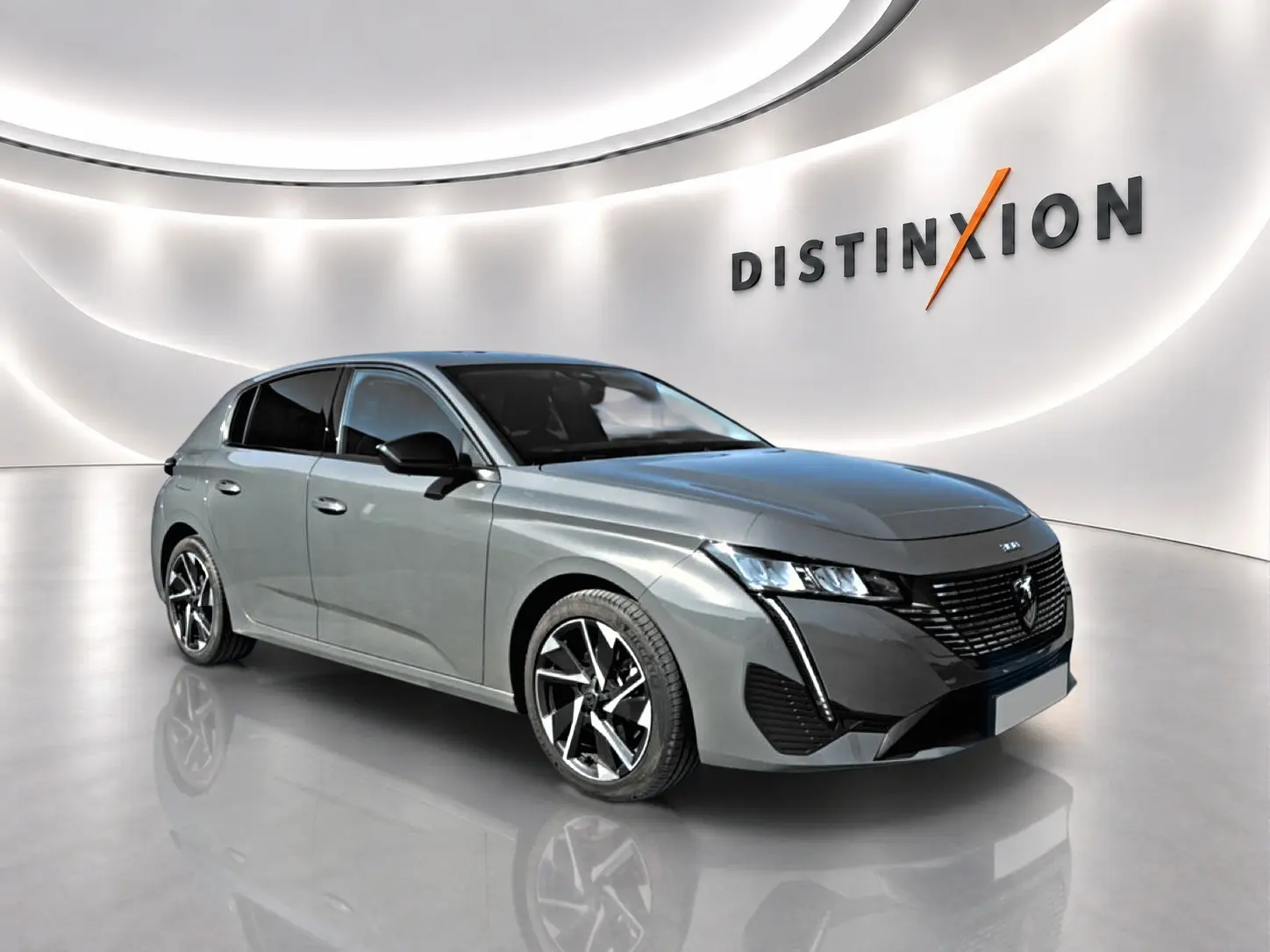 Peugeot 308 gris vue 3/4 avant droit, jantes alu noires et phares LED dans un showroom lumineux.