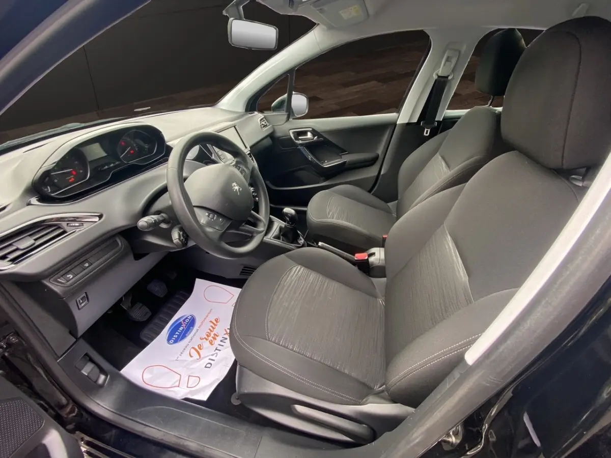 Vue intérieure côté conducteur de la Peugeot 208 Affaire noire, montrant les sièges et le tableau de bord avec volant multifonctions.