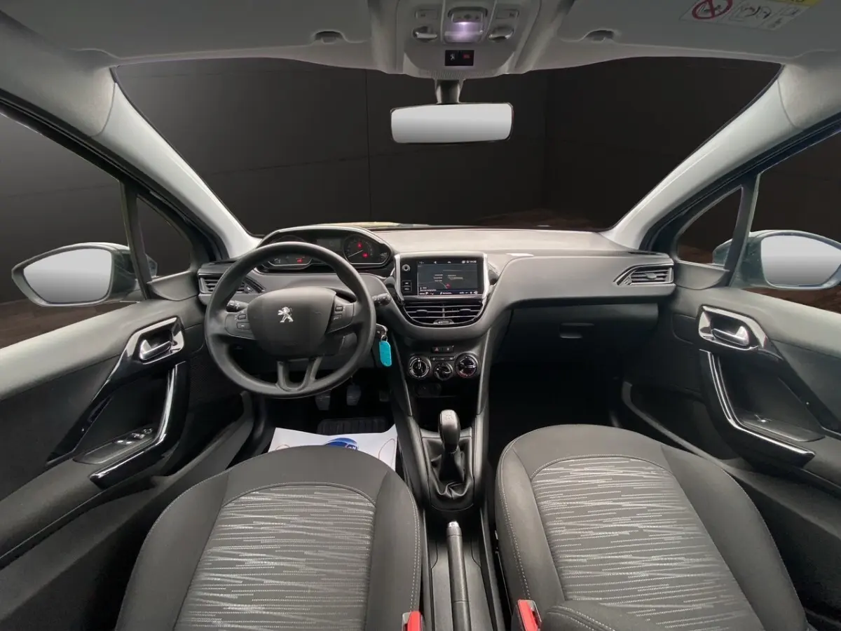 Vue intérieure avant de la Peugeot 208 Affaire noire, montrant le tableau de bord, volant multifonctions et sièges tissu gris.