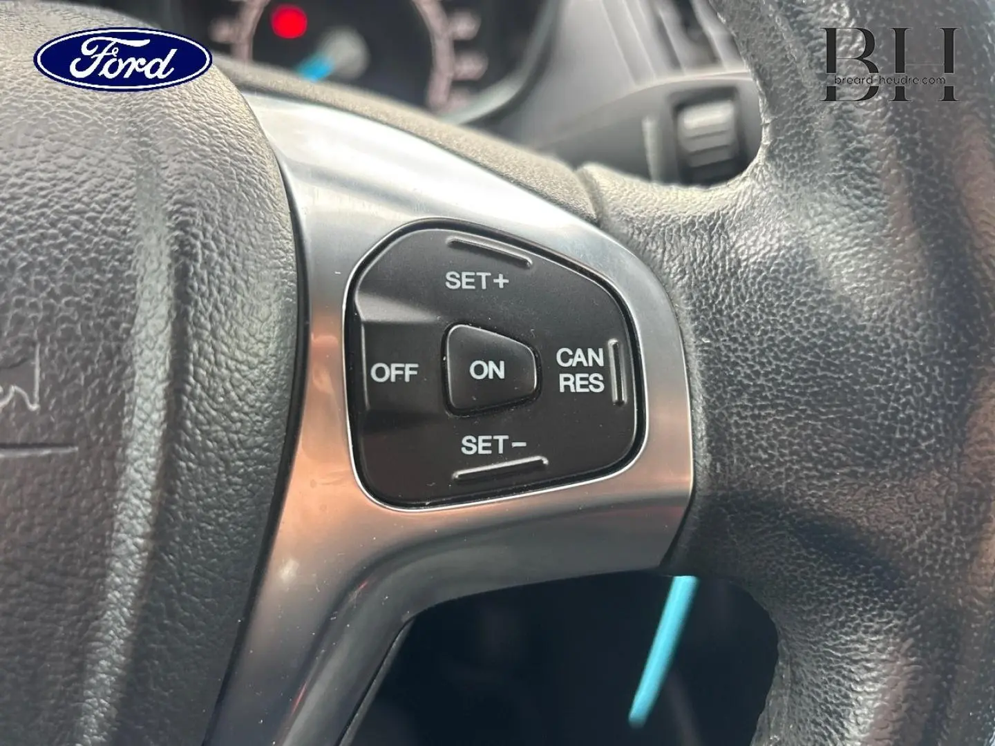 Gros plan sur les commandes du régulateur de vitesse au volant cuir d'une Ford B-MAX rouge Premium Candy.