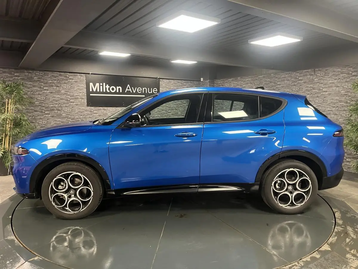 Profil côté gauche de l'Alfa Romeo Tonale Sprint 2024 bleu métallisé avec jantes alliage 18 pouces en intérieur showroom.