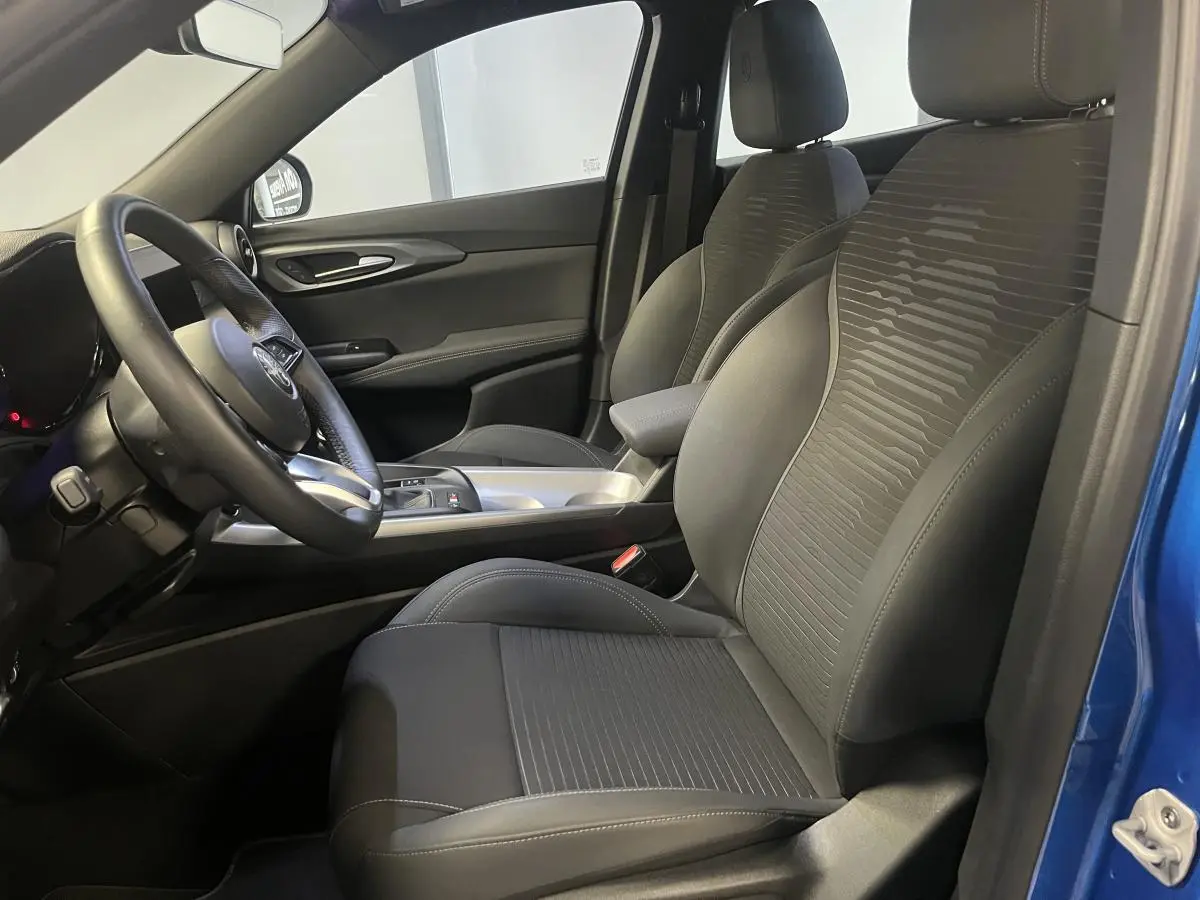 Vue intérieure côté conducteur de l'Alfa Romeo Tonale bleu, avec sièges tissu noir et volant sport cuir.