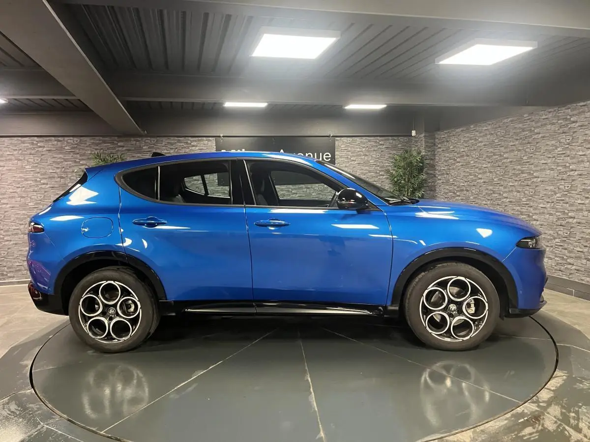 Profil côté gauche d'un Alfa Romeo Tonale Sprint 2024 bleu métallisé avec jantes noires en intérieur showroom.