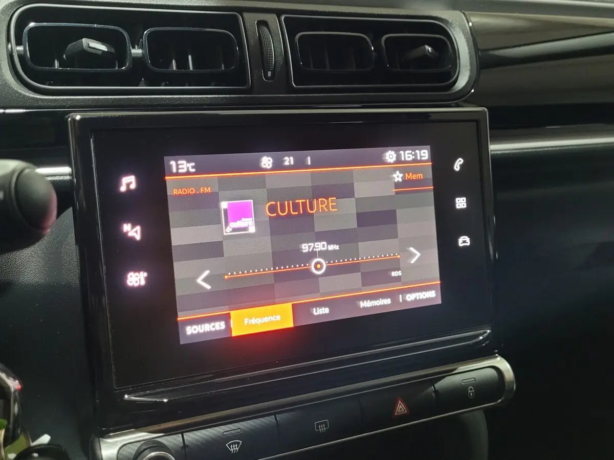 Écran tactile central allumé montrant radio FM dans l'habitacle noir d'une Citroën C3 beige de 2022.