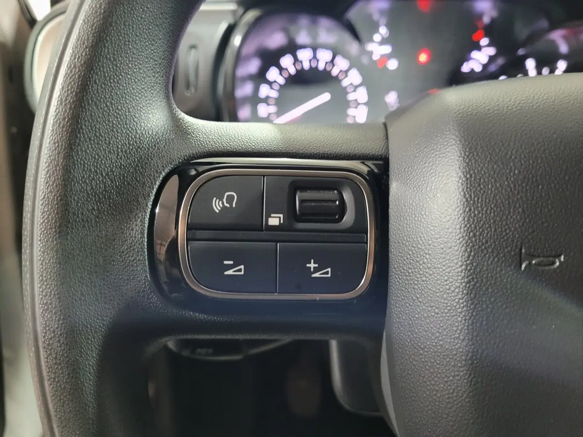 Gros plan sur les commandes du volant côté gauche de la Citroën C3 beige PureTech 2022 avec tableau de bord flou en arrière-plan.