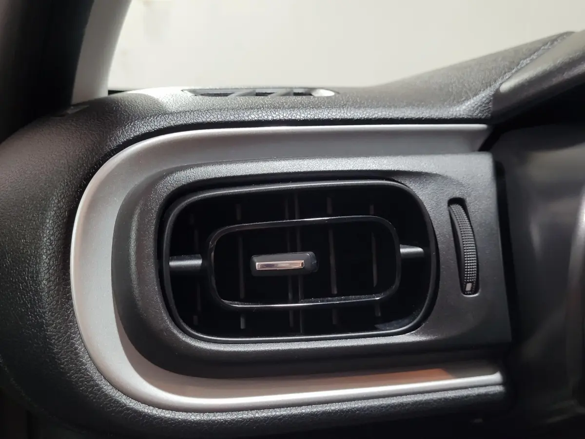 Gros plan sur la sortie d'air rectangulaire noire avec contour argenté du tableau de bord d'une Citroën C3 beige.