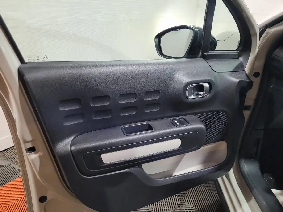 Vue rapprochée de la porte avant gauche beige de la Citroën C3 avec son panneau intérieur noir et beige et commandes électriques.