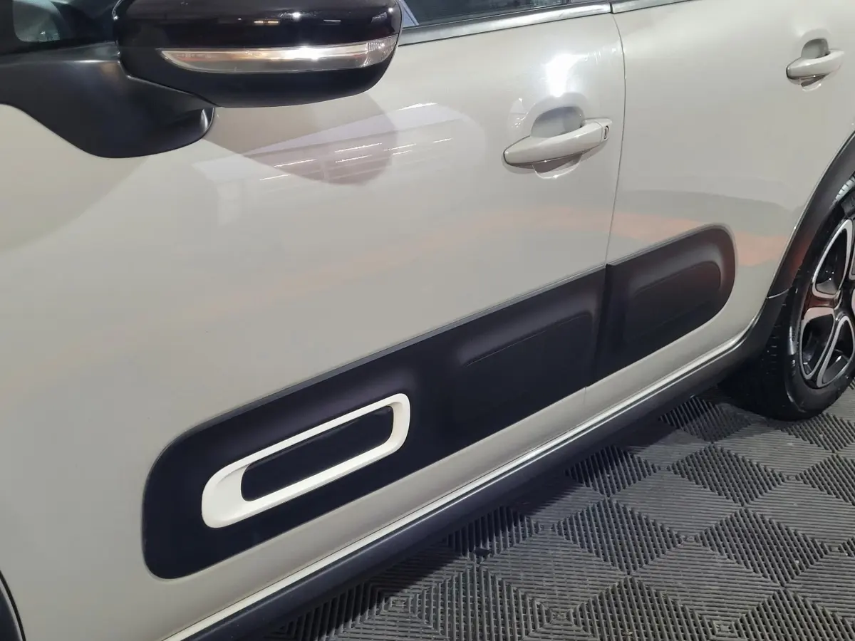 Gros plan sur la porte côté gauche beige d'une Citroën C3 2022 avec protection noire distinctive et rétroviseur noir.