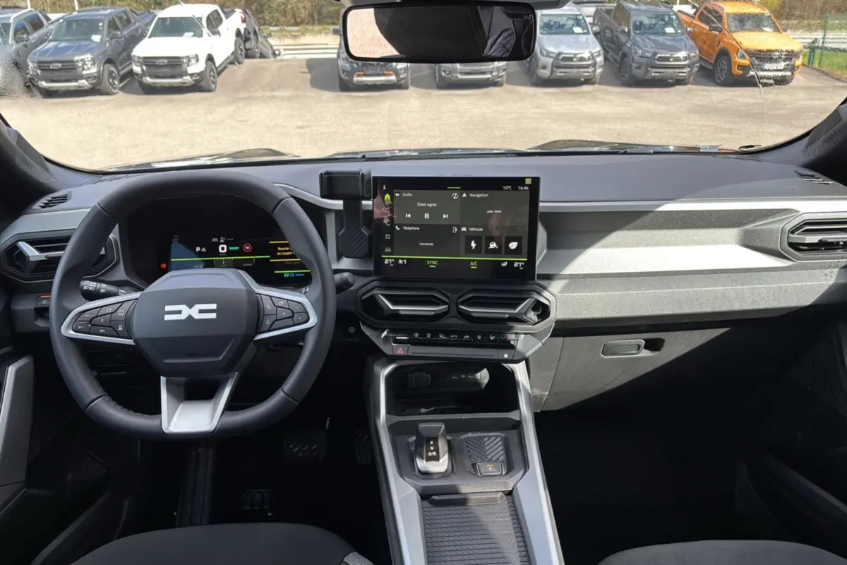 Vue intérieure avant du tableau de bord du Dacia Bigster Hybrid 155 avec écran tactile et volant cuir noir.
