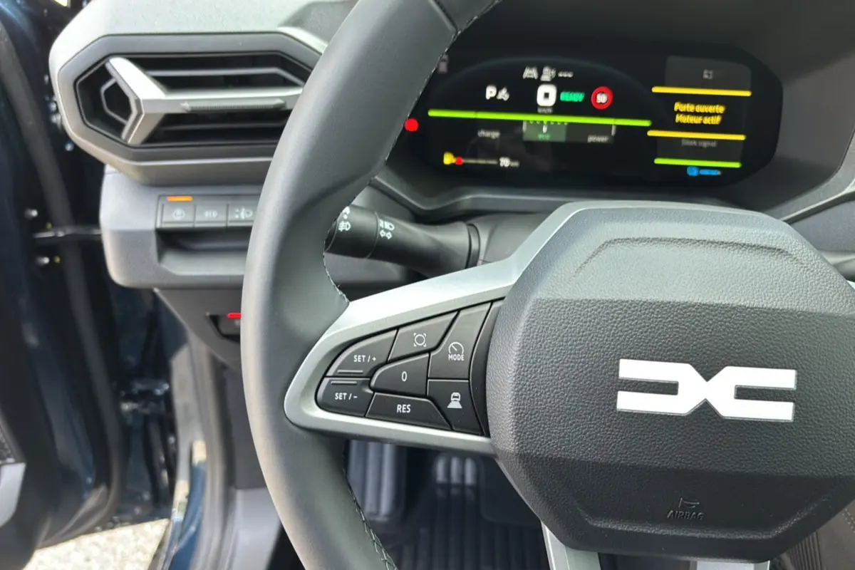 Gros plan sur le volant cuir et tableau de bord digital du Dacia Bigster Hybrid 155 bleu indigo avec portes ouvertes.