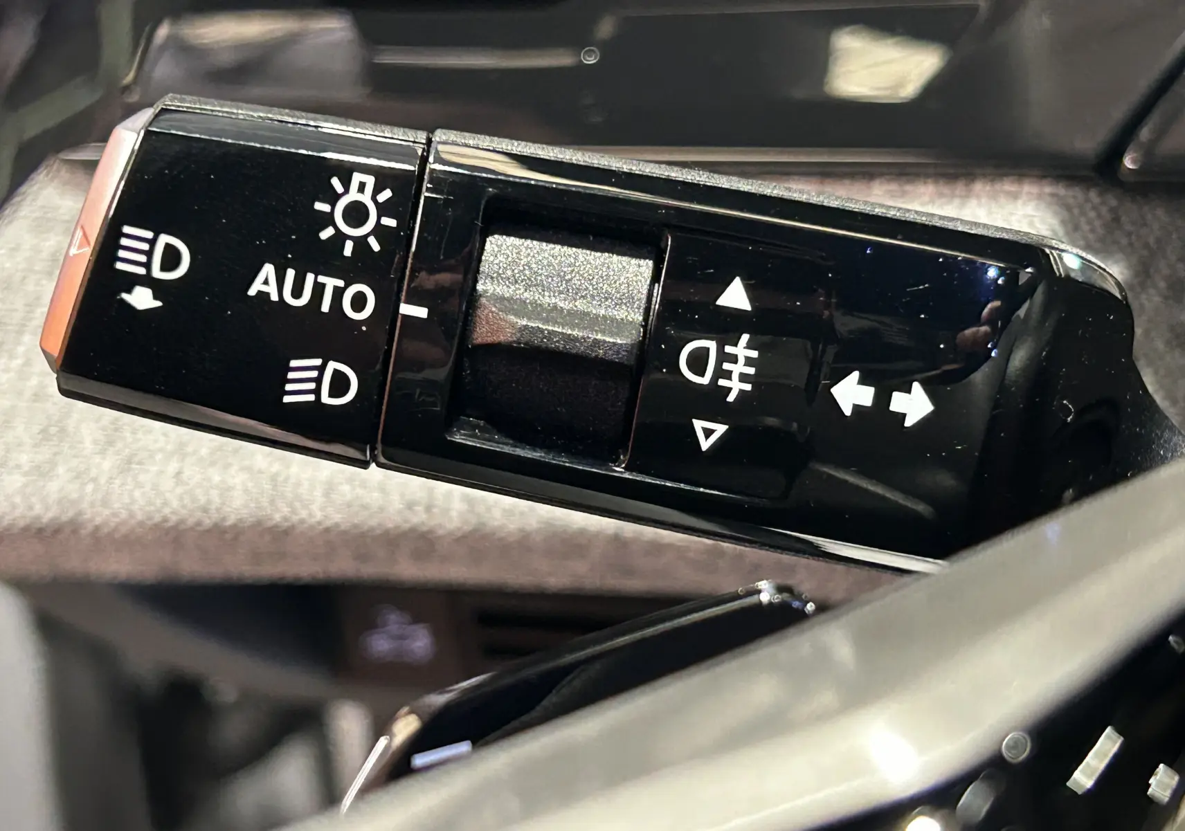 Gros plan sur la commande des feux et clignotants du Peugeot 3008 III Hybrid 145, intérieur noir brillant.
