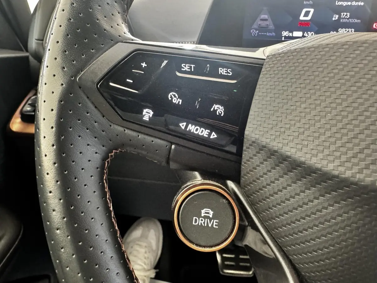 Gros plan sur le volant cuir perforé noir du Cupra Born 230ch avec commandes multifonctions et bouton Drive.