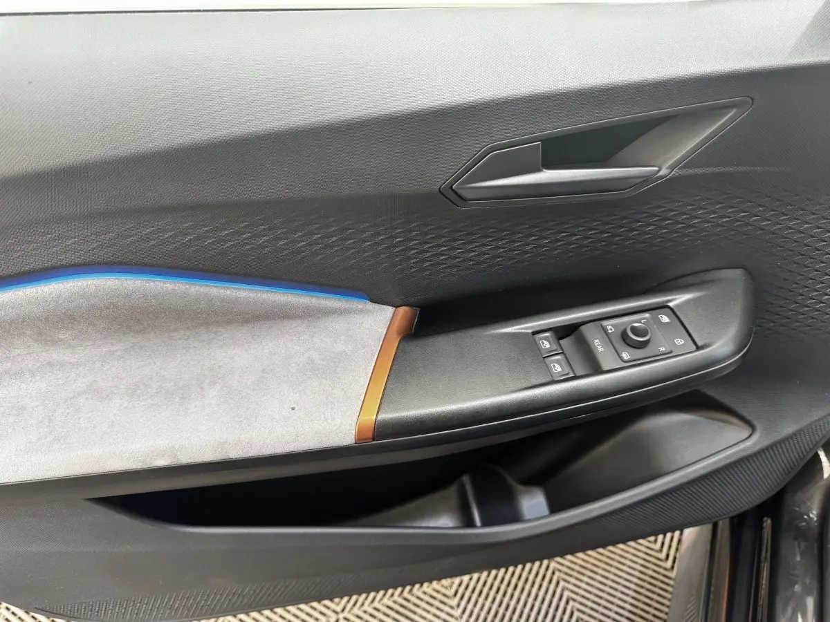 Vue intérieure côté gauche de la porte d’une CUPRA Born 230ch gris foncé avec insert bleu et commandes de vitres.