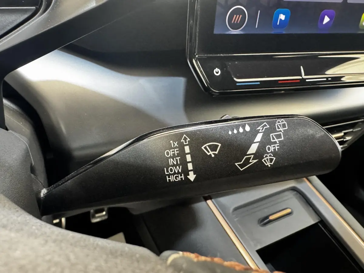 Gros plan sur la commande des essuie-glaces dans l’habitacle sombre d’une CUPRA BORN gris foncé, écran tactile en arrière-plan.