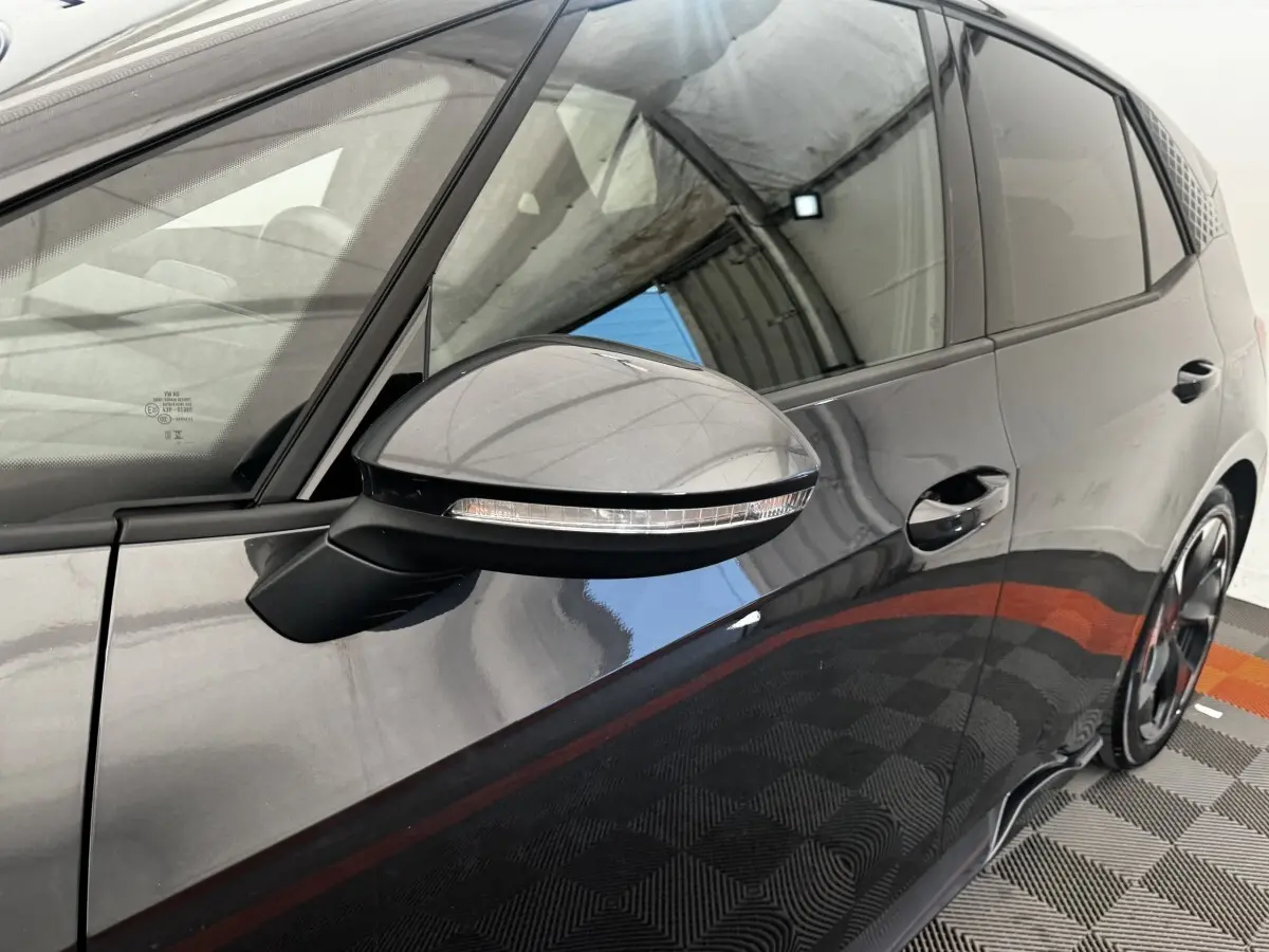 Gros plan sur le rétroviseur côté gauche et la portière gris foncé d'une CUPRA BORN 230ch, reflet du plafond visible.