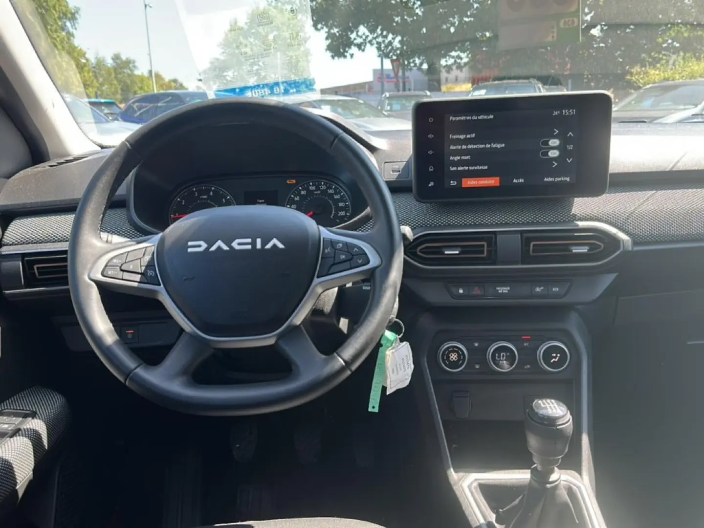 Vue intérieure frontale du tableau de bord et volant noir de la Dacia Sandero 2025 avec écran tactile et boîte manuelle.