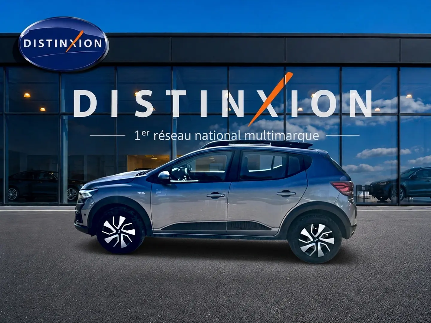 Profil droit de la Dacia Sandero Stepway gris schiste 2025 avec barres de toit et enjoliveurs noirs et argentés.