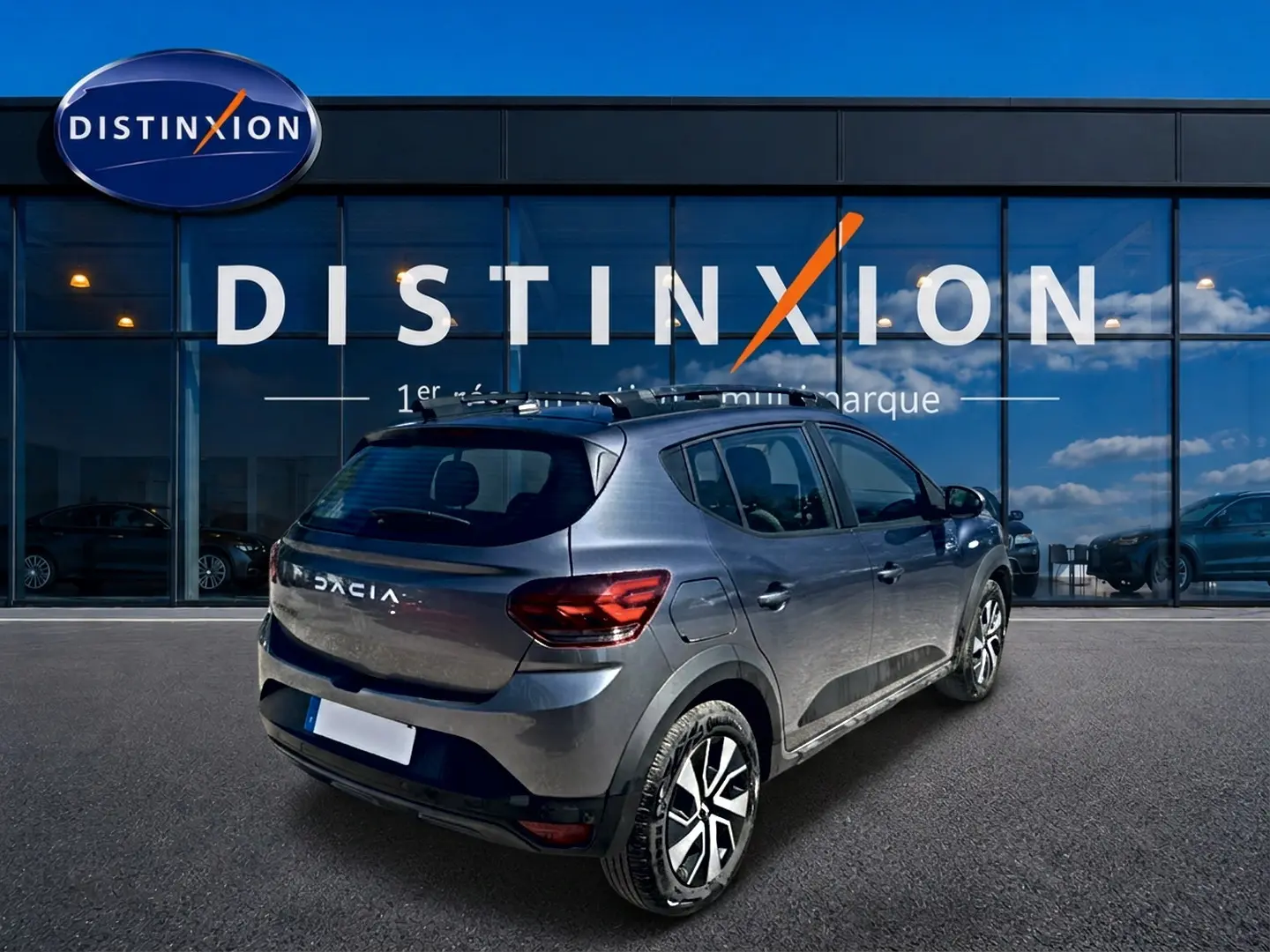Vue 3/4 arrière droite d'une Dacia Sandero Stepway gris schiste avec barres de toit et jantes alliage noires.