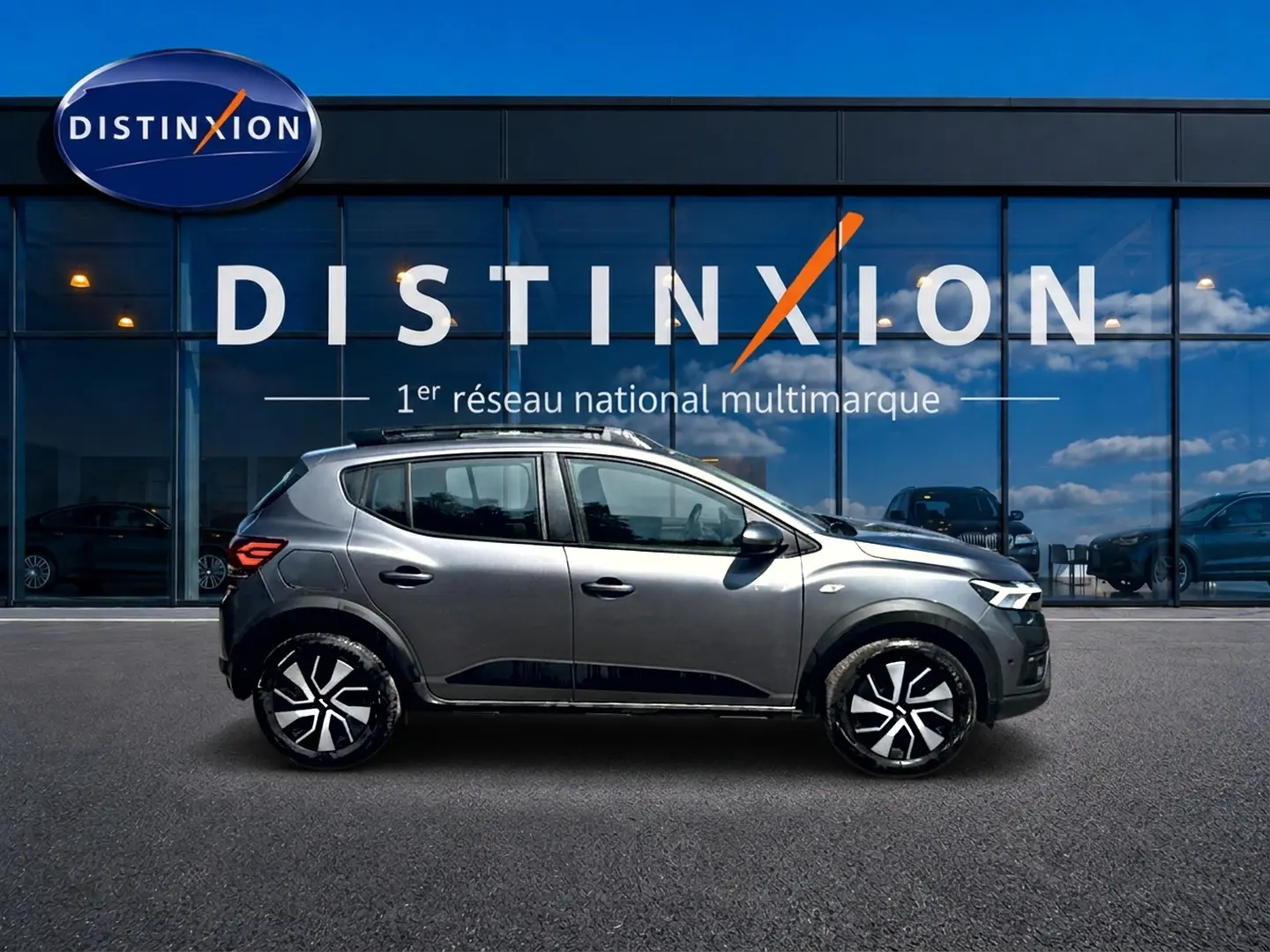 Profil droit d'une Dacia Sandero Stepway gris schiste 2025 avec barres de toit et jantes noires stylisées.