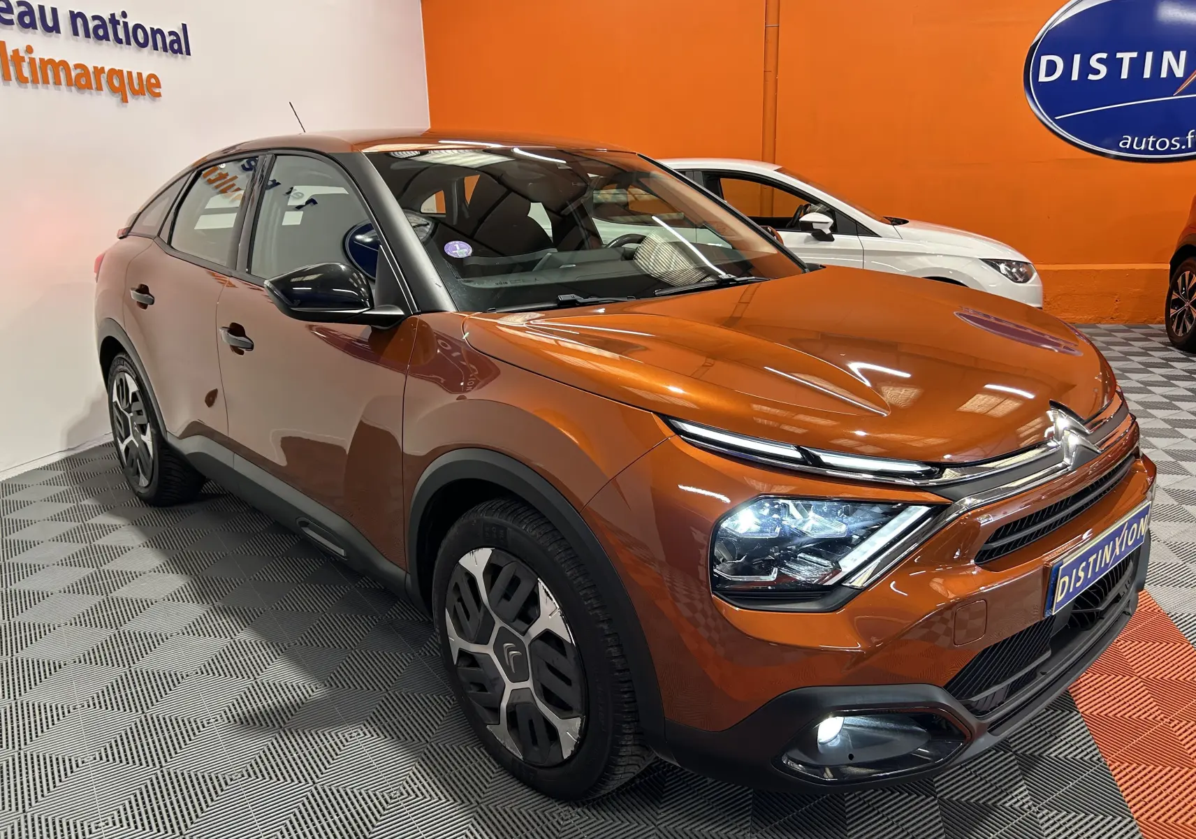 Vue 3/4 avant d'une Citroën C4 PureTech 100 Feel orange avec attelage et caméra, dans un showroom lumineux.