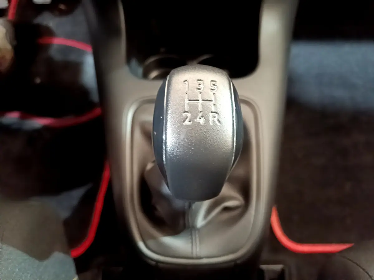 Le levier de vitesses manuel gris de la Citroën C3 PureTech 68 BVM Live vu de dessus, entouré de tapis noirs avec surpiqûres rouges.