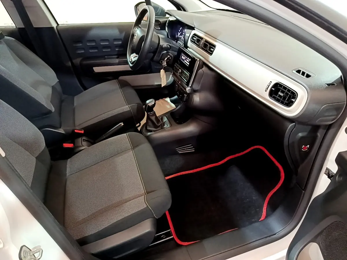 Intérieur avant droit d'une Citroën C3 blanche 2018, sièges gris, tableau de bord clair et tapis noir à bordure rouge.