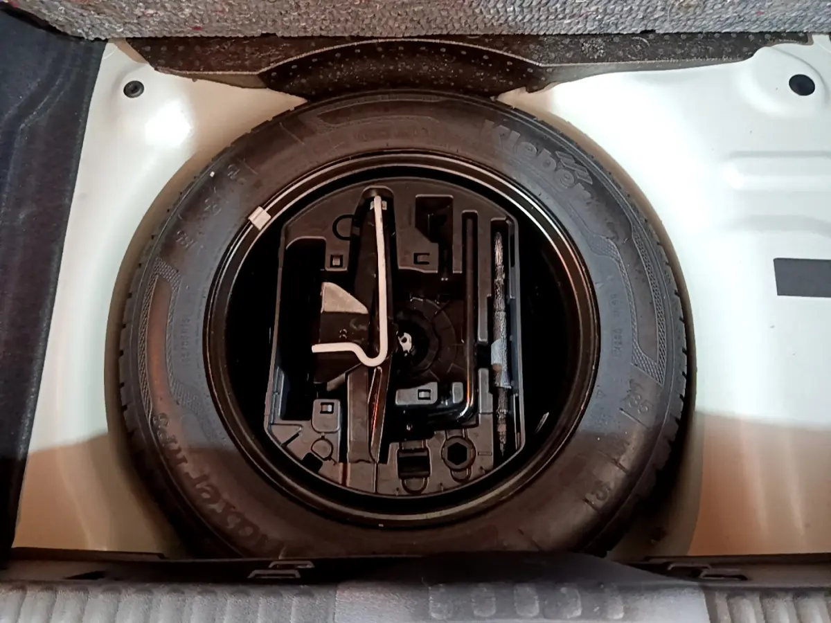 Vue plongeante sur la roue de secours noire et son compartiment blanc dans le coffre d'une Citroën C3 blanche.