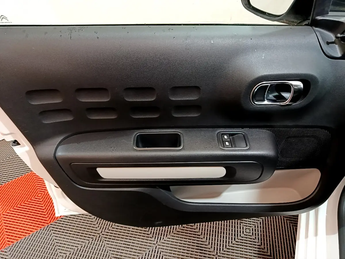 Vue rapprochée de la porte côté gauche d'une Citroën C3 blanche, avec poignée intérieure chromée et commandes de vitres.