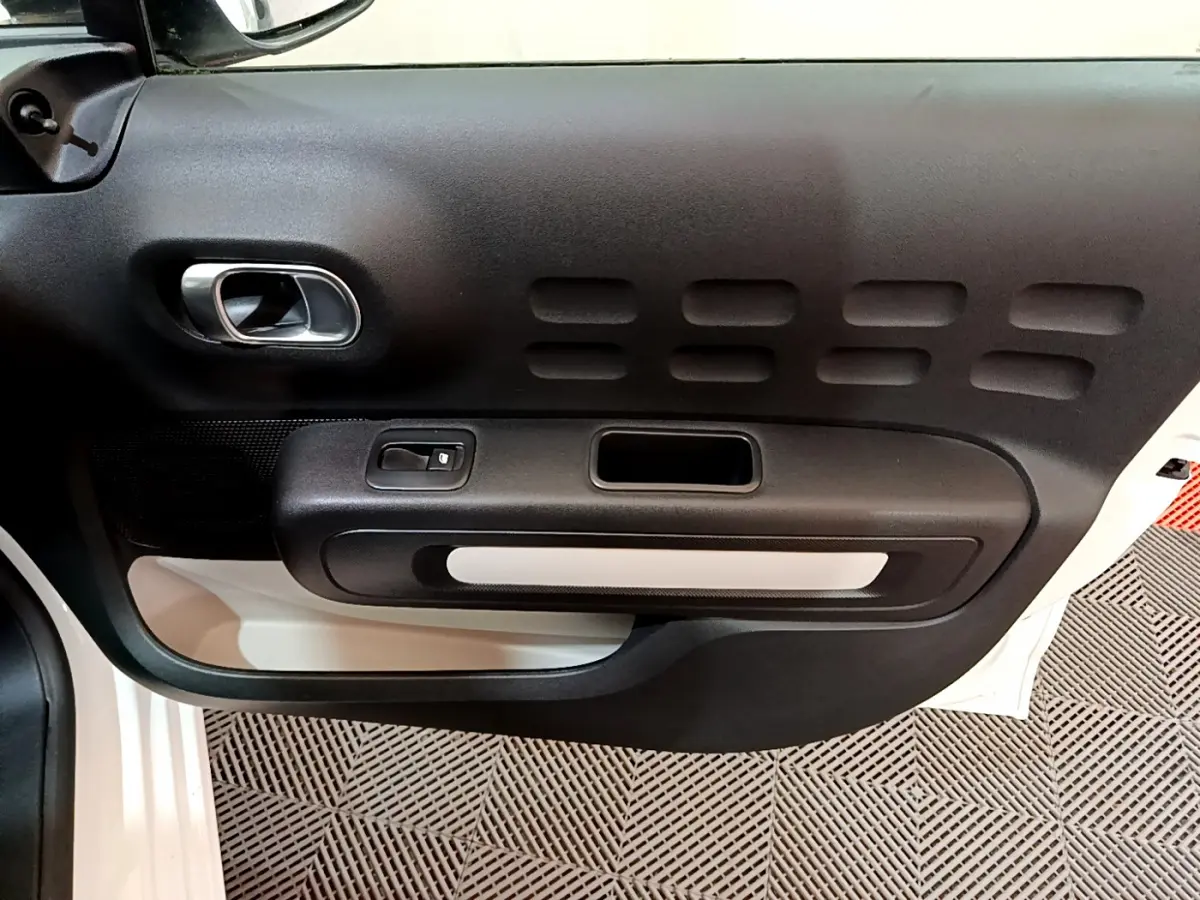 Vue rapprochée de la porte côté gauche de la Citroën C3 blanche, mettant en valeur la poignée intérieure et le bouton de lève-vitre.