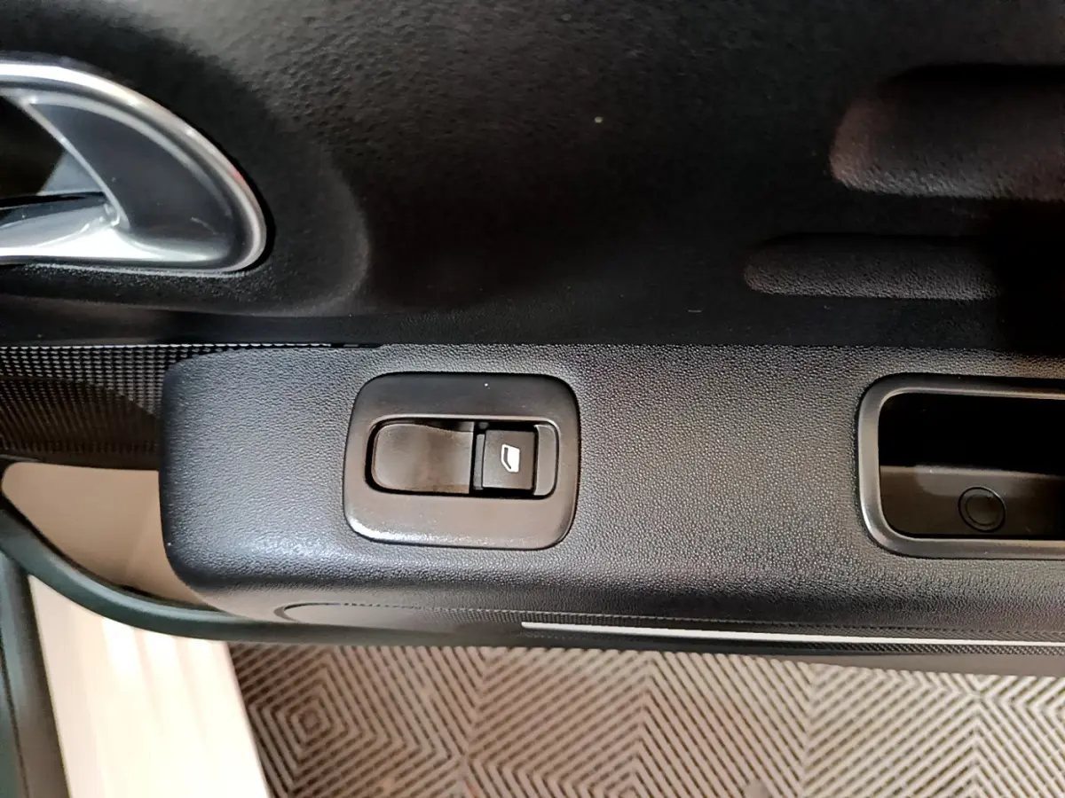 Gros plan sur le bouton de commande de la vitre électrique côté gauche de la porte intérieure noire d'une Citroën C3 blanche.