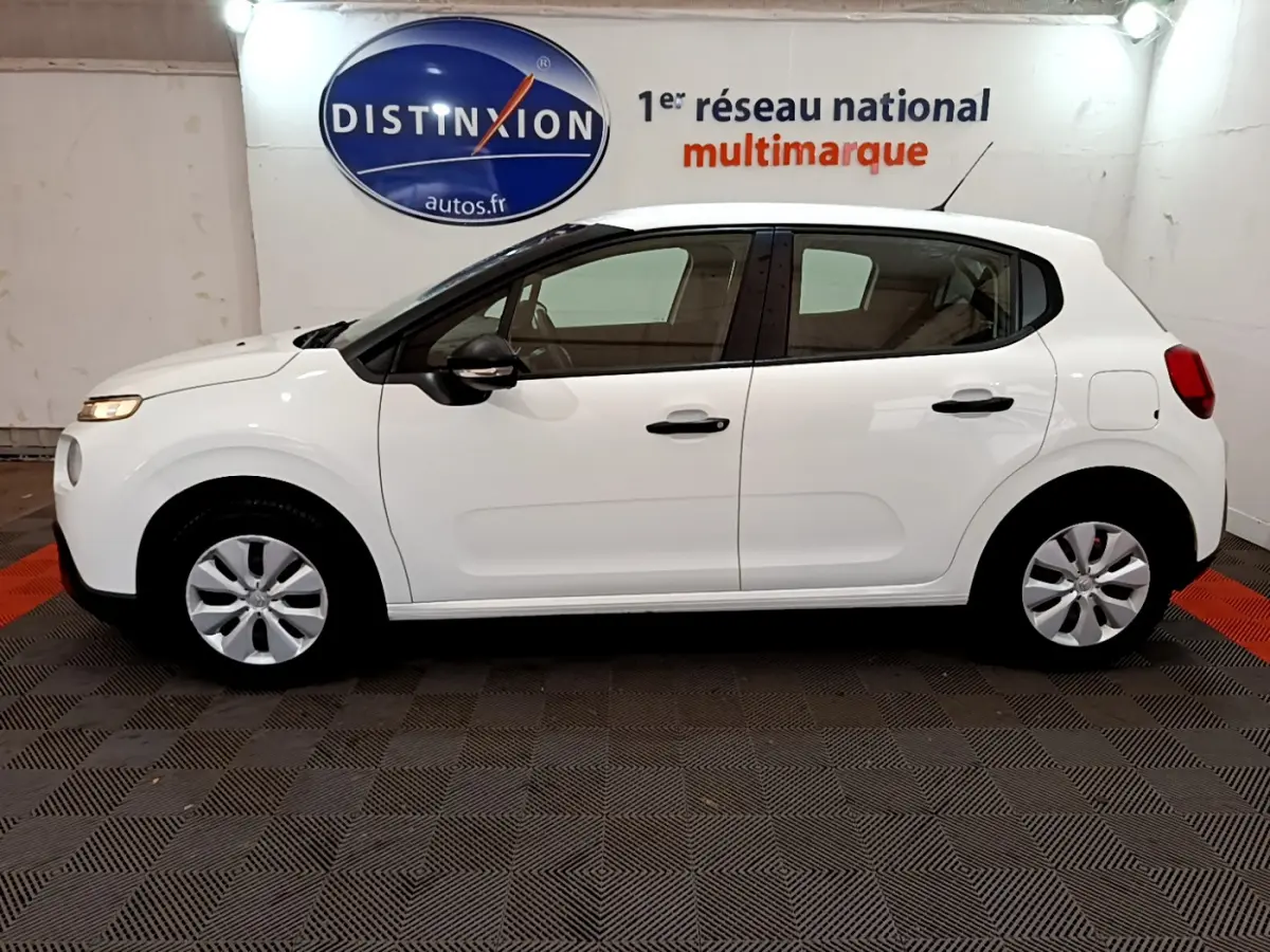 Profil latéral gauche d'une Citroën C3 blanche 2018, avec poignées et rétroviseurs noirs dans un showroom.