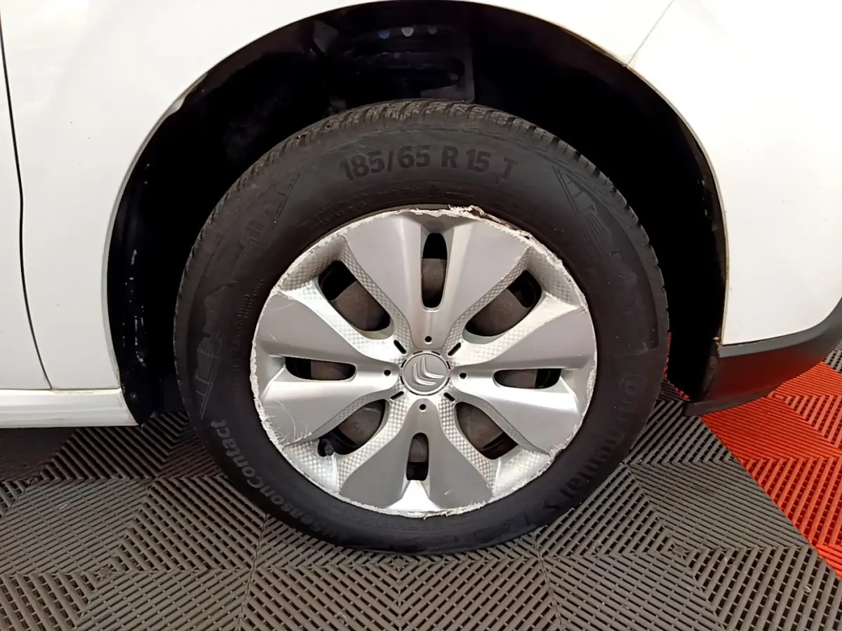 Gros plan sur la roue avant gauche d'une Citroën C3 blanche avec enjoliveur endommagé visible.