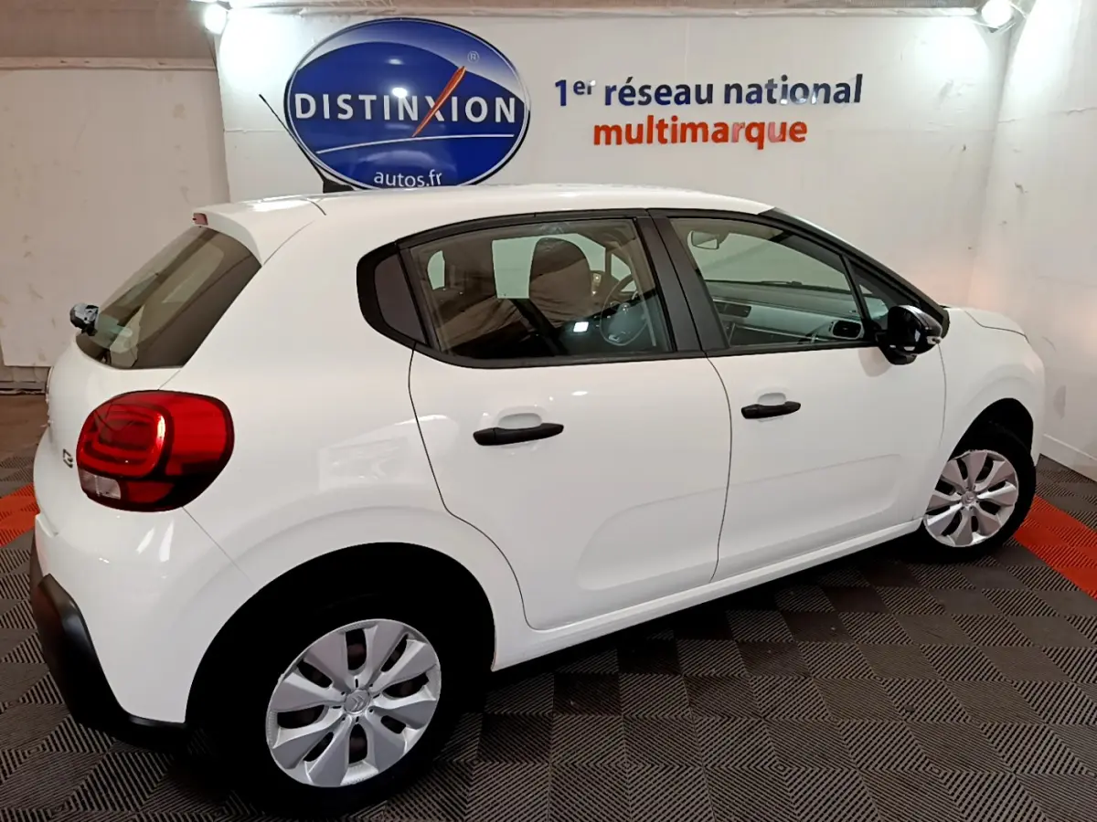 Citroën C3 blanc vue de profil côté droit en intérieur avec jantes argentées et feux arrière rouges.