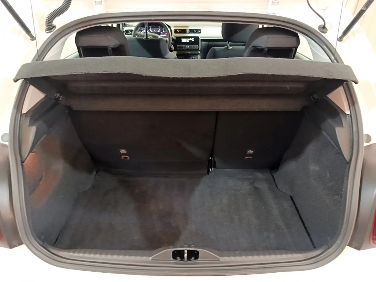 Coffre ouvert vu de l'arrière d'une Citroën C3 blanche avec banquette arrière noire et tablette de coffre relevée.
