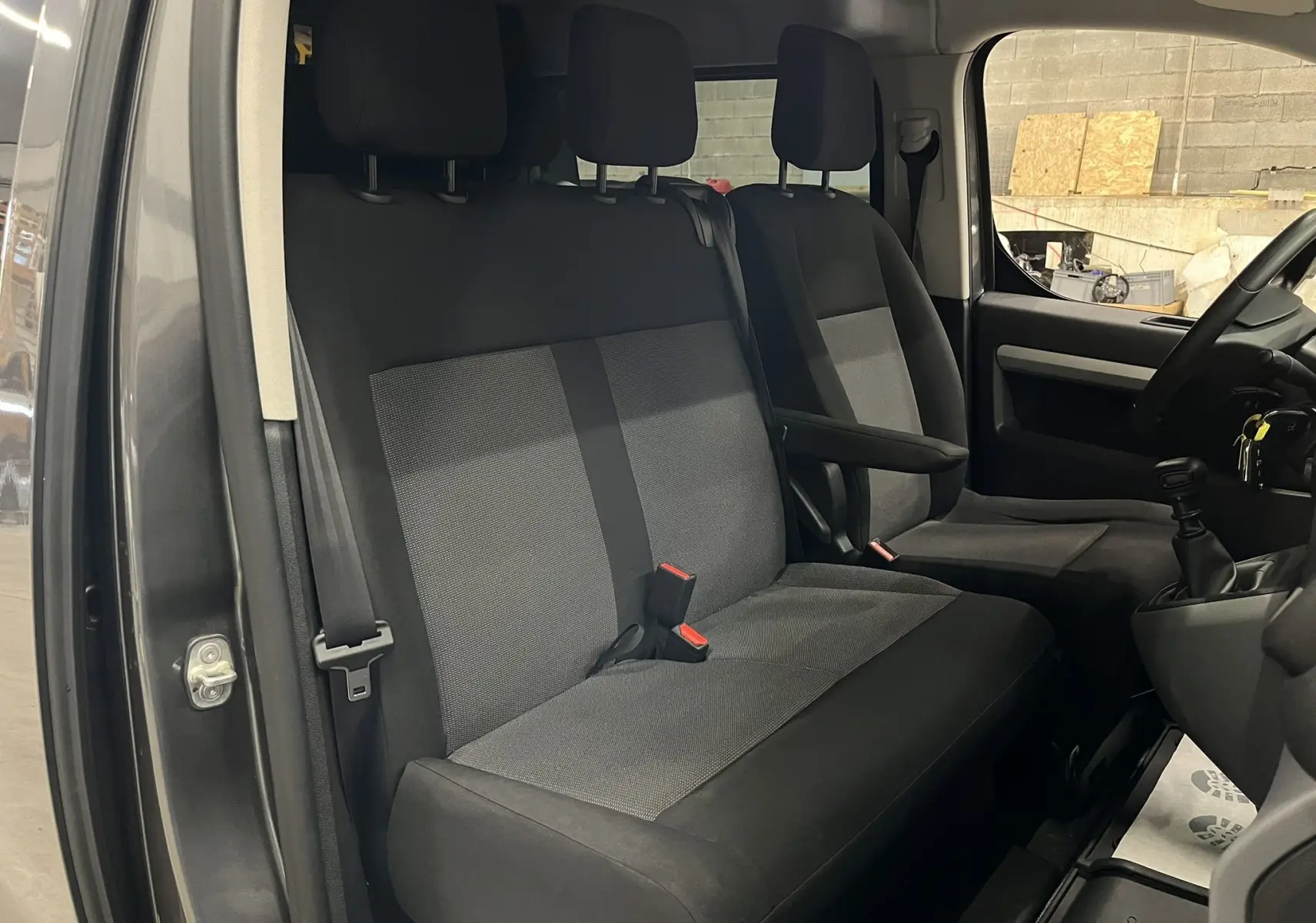 Vue intérieure côté conducteur de l’Opel Vivaro XL gris 2023, montrant les sièges tissu noirs et la boîte manuelle.