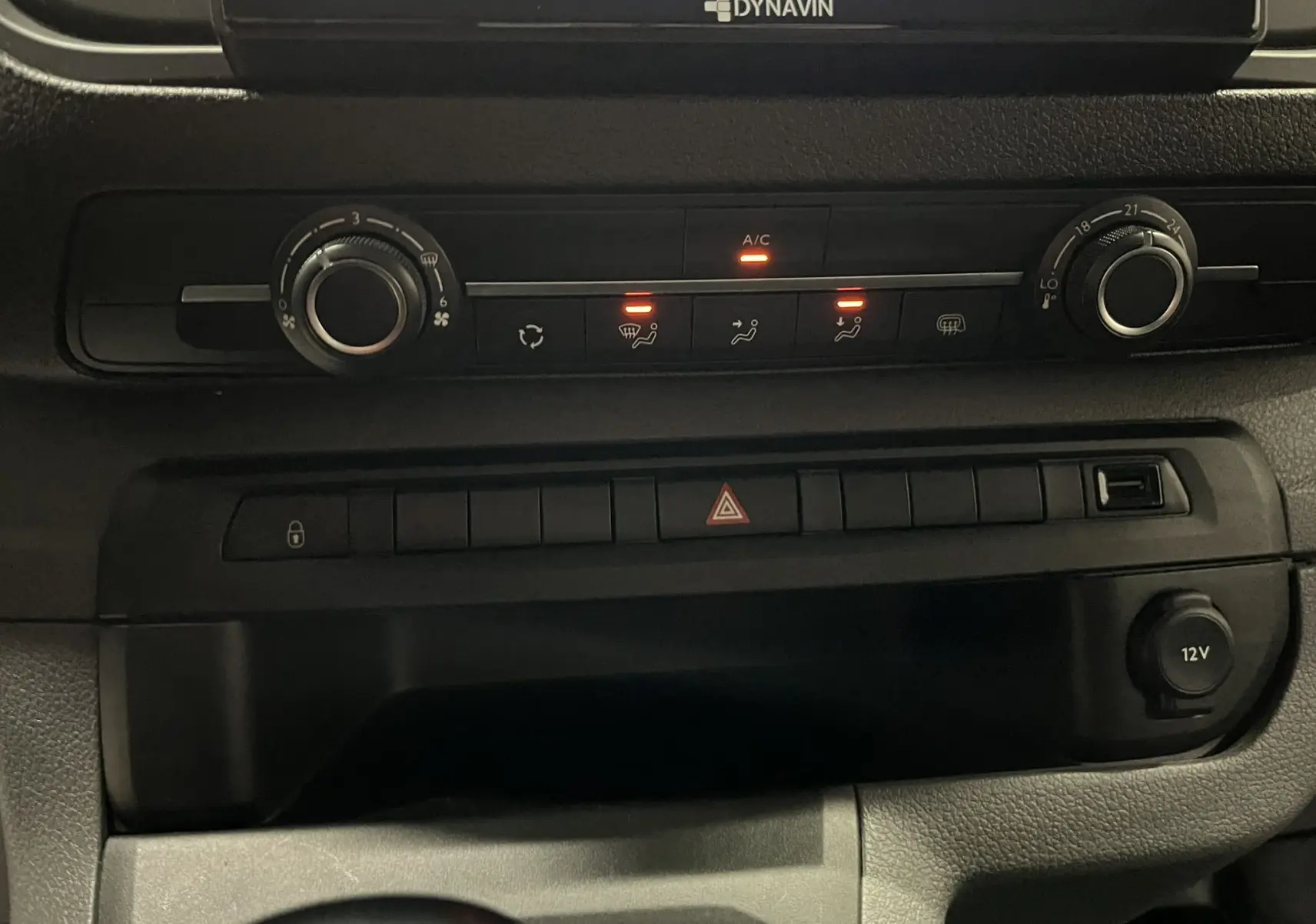 Vue rapprochée du tableau de bord noir de l'Opel Vivaro XL 2023, montrant les commandes de climatisation et prises 12V.