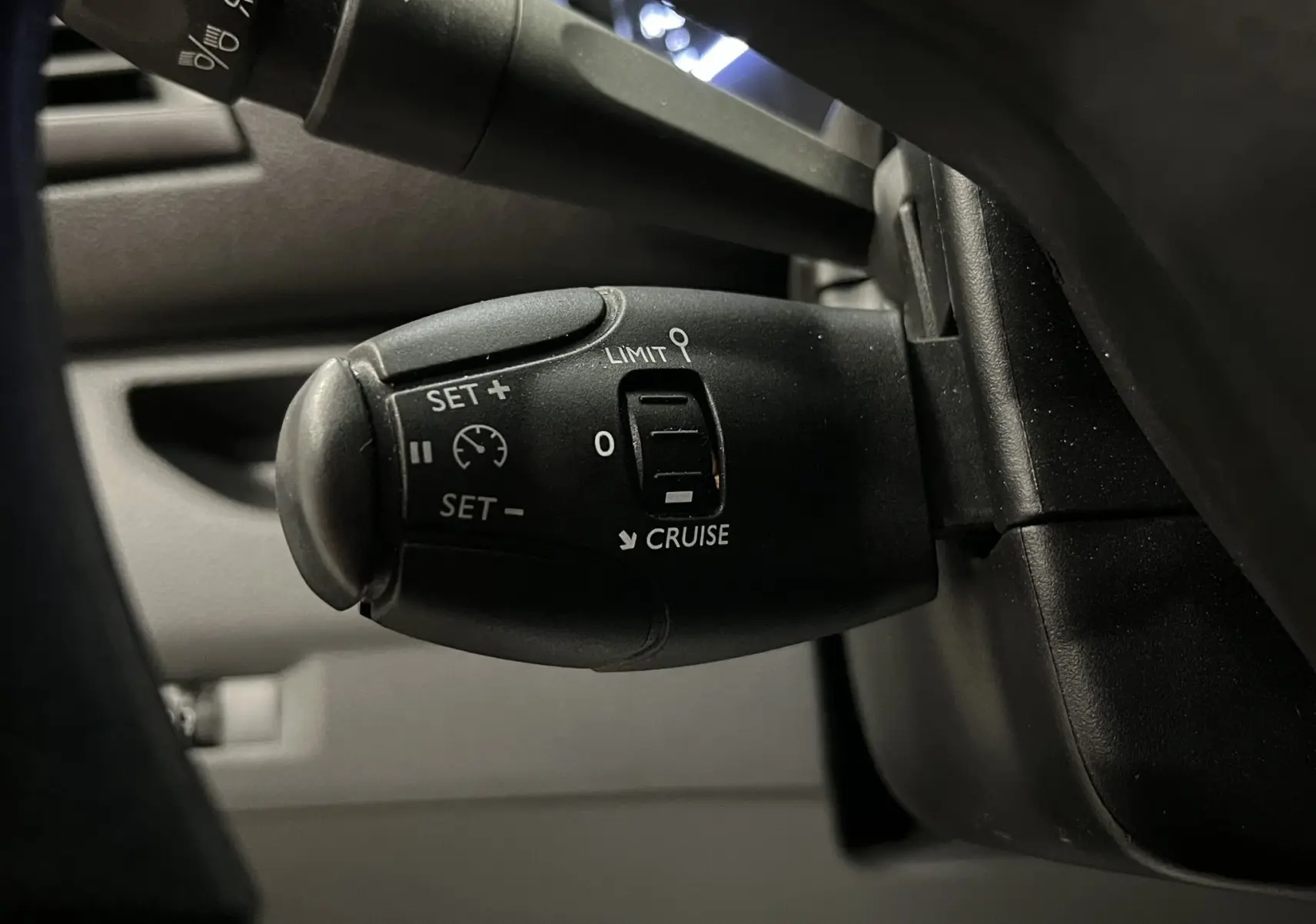 Gros plan sur la commande de régulateur de vitesse noire à gauche du volant dans l'habitacle gris de l'Opel Vivaro XL 2023.