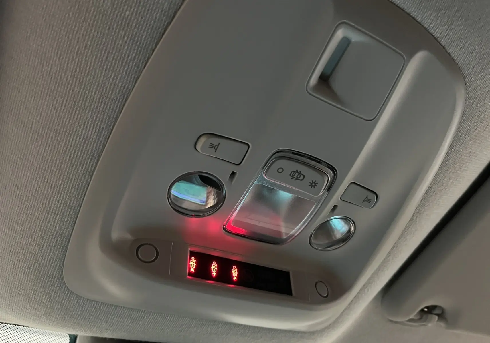 Vue en contre-plongée du plafonnier gris clair de l'Opel Vivaro XL avec commandes d'éclairage et voyants rouges allumés.