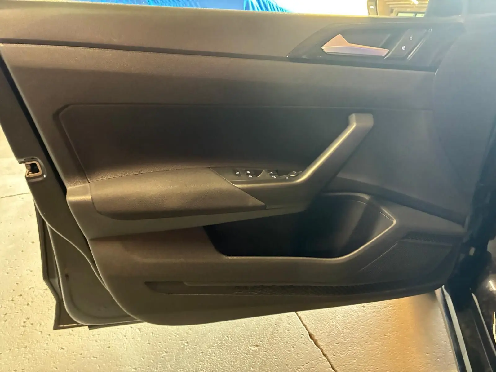 Vue intérieure du panneau de porte côté conducteur de la Volkswagen Polo noire 2022 avec commandes des vitres électriques.