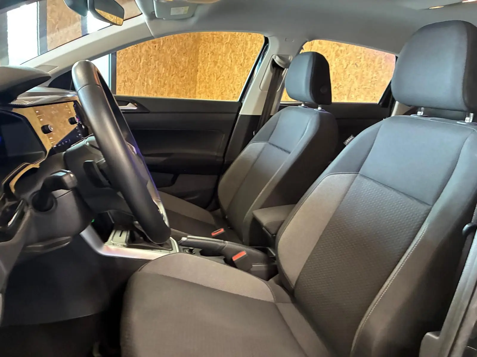 Vue intérieure côté conducteur de la Volkswagen Polo 2022, sièges tissu gris noir et volant multifonctions cuir.