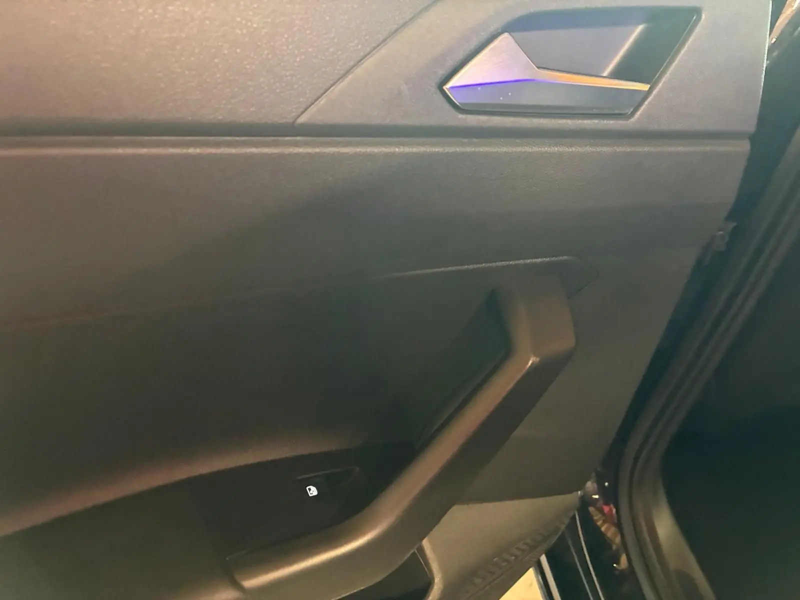 Détail de la poignée intérieure côté droit de la porte arrière d'une Volkswagen Polo noire avec bouton de verrouillage.