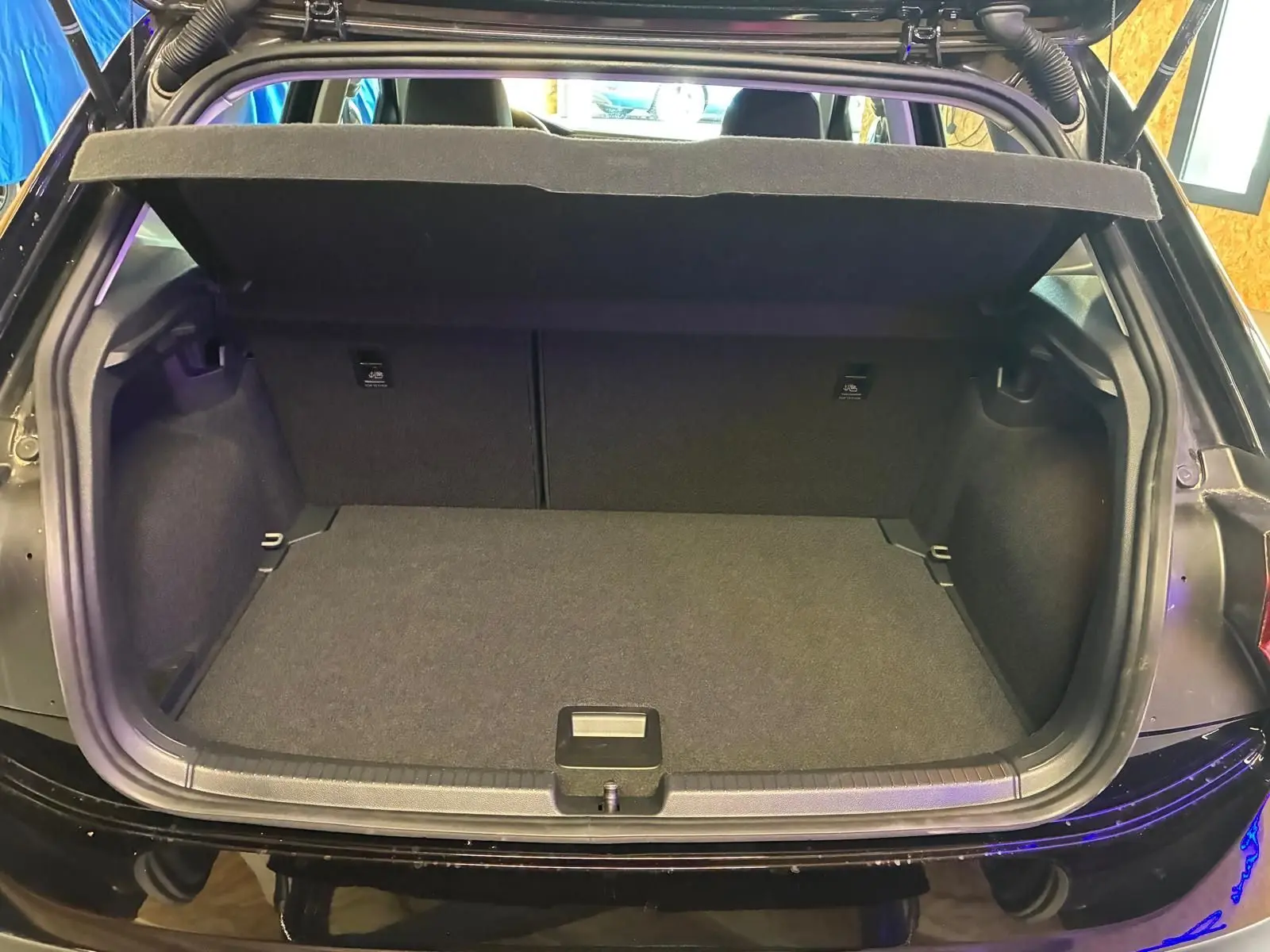 Coffre ouvert vu de l'arrière d'une Volkswagen Polo noire 5 portes, intérieur du coffre tapissé de tissu gris foncé.