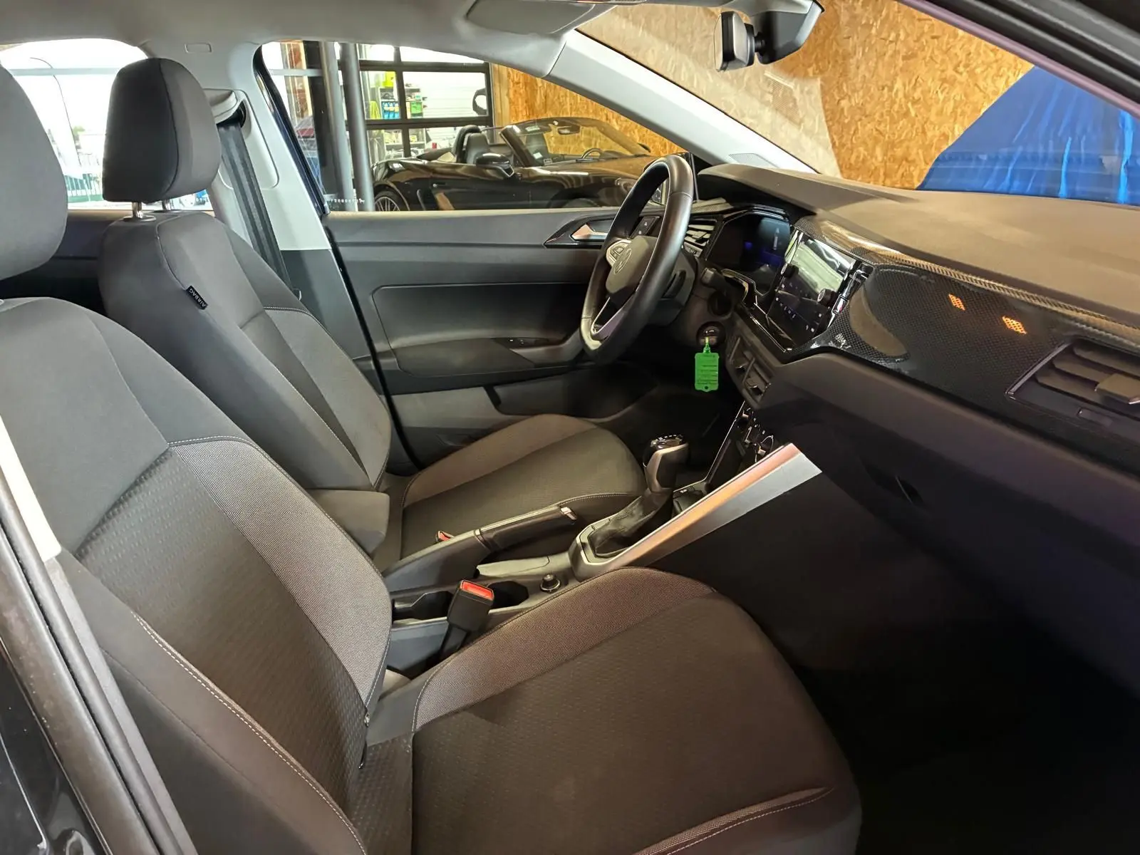 Vue intérieure côté conducteur de la Volkswagen Polo 1.0 TSI noire avec sièges tissu gris et tableau de bord moderne.
