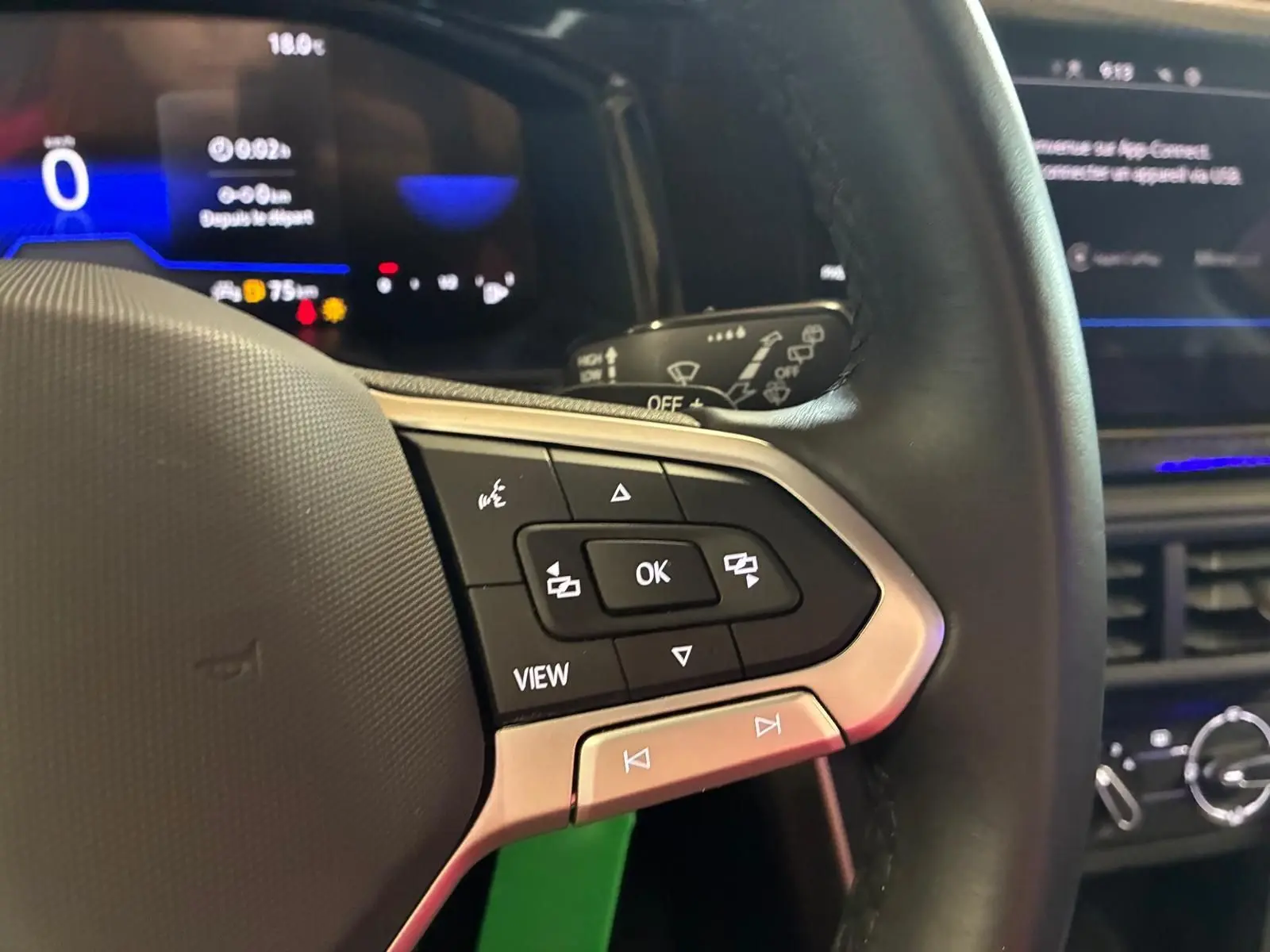 Gros plan sur le volant cuir noir de la Volkswagen Polo 2022, avec commandes multifonctions et tableau de bord numérique bleu.