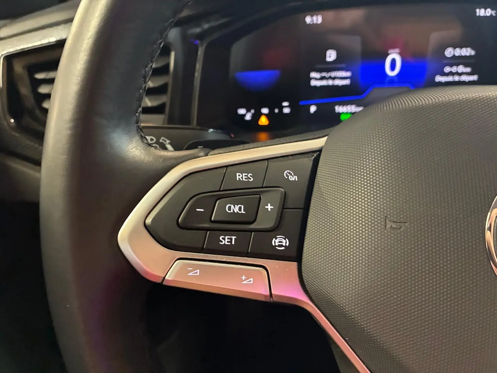 Gros plan sur les commandes du régulateur de vitesse au volant cuir d'une Volkswagen Polo noire, tableau de bord numérique en arrière-plan.